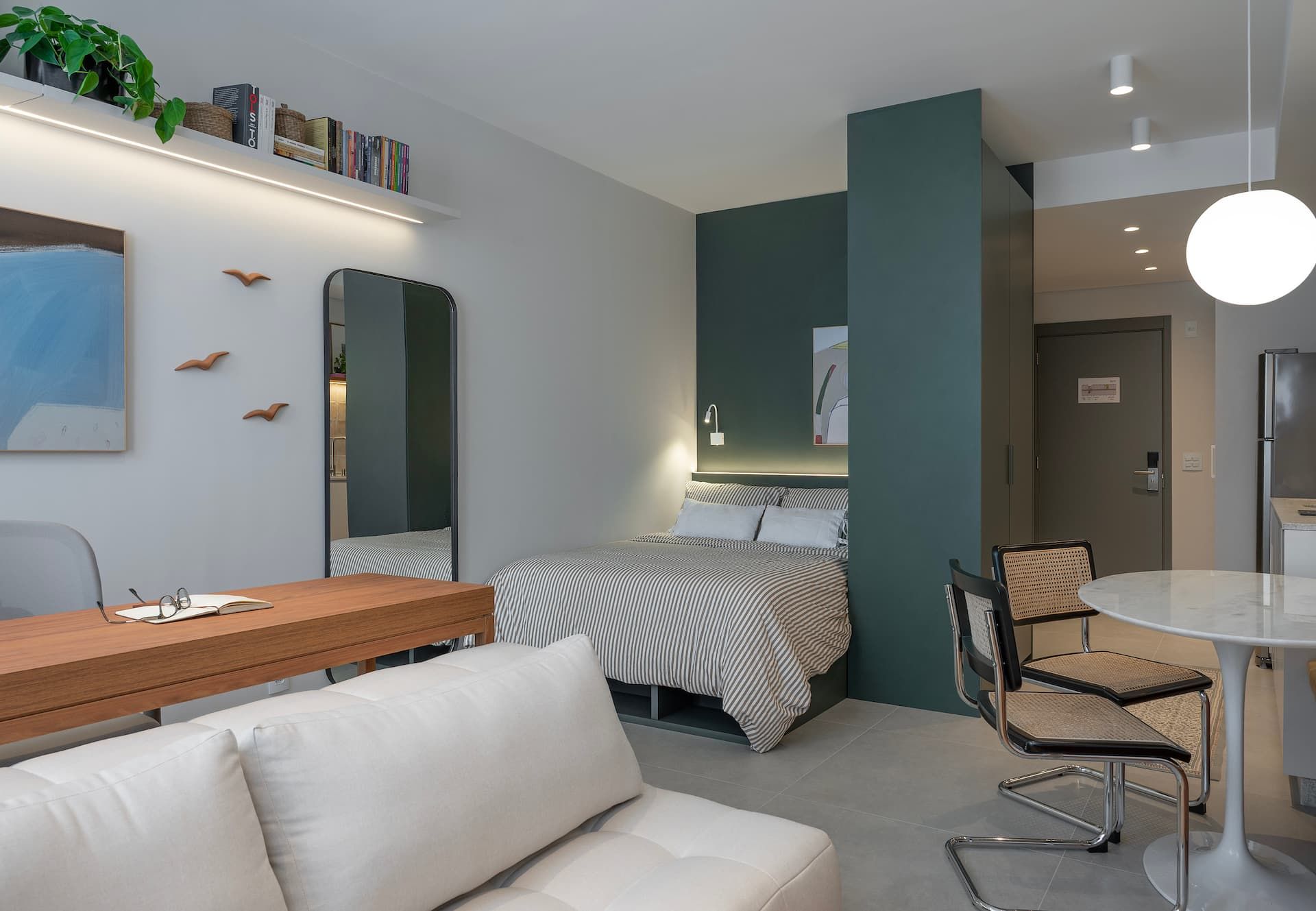 Vista geral do studio com sofá, mesa de jantar e cama de casal